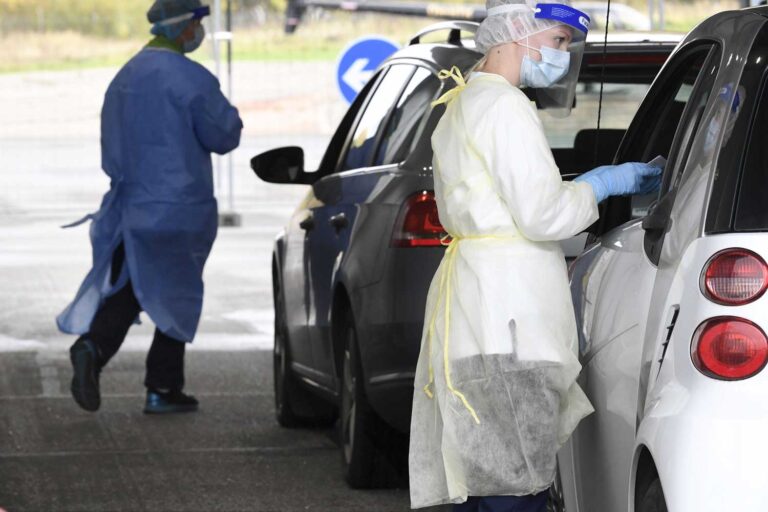 Suojavarusteisiin pukeutuneet hoitajat ottavat koronavirusnäytteitä autolla testaukseen saapuneilta.