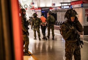 Maastopukuiset sotilaat harjoittelevat metroasemalla. Kiinniotettavaa esittävää siviiliä talutetaan pois kädet sidottuina.