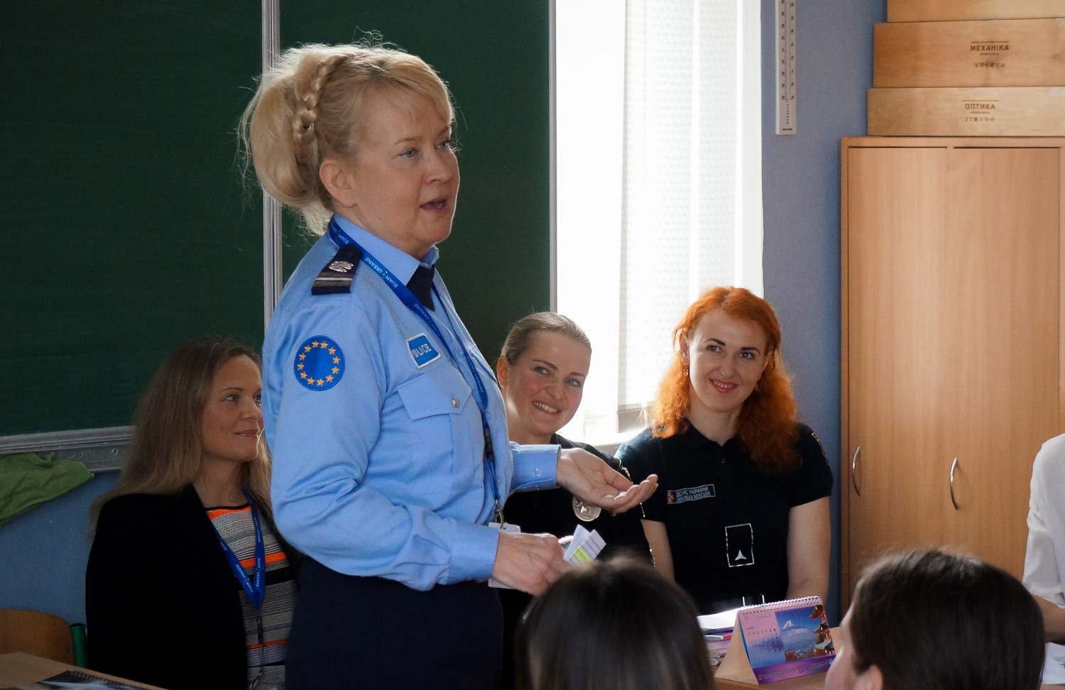 Suomalainen naispoliisi pitämässä koulutusta. Taustalla oppilaita.
