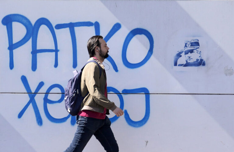 Kävelevän miehen takana seinässä on graffiti, jossa lukee Ratko on sankari ja viereen on sapluunalla maalattu Ratkon kuva.