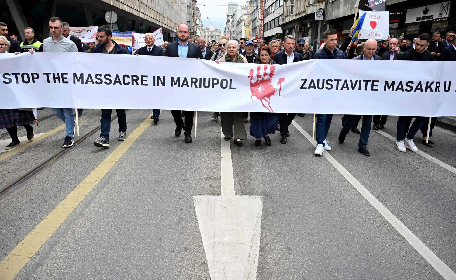 Mielenosoittajat kävelevät kadulla kädessään banderolli, jossa lukee "Stop the massacre in Mariupol".