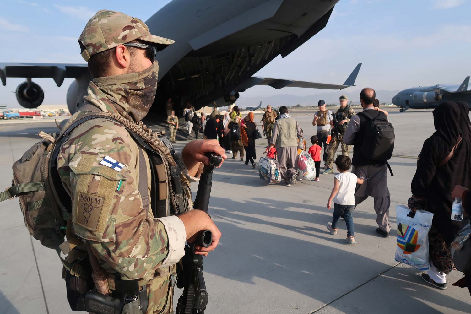 Suomalainen sotilas seuraa, kun afganistanilaiset kävelevät Kabulin lentokentällä kohti kuljetuskonetta.