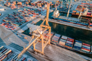 Talvisessa maisemassa värikkäiden konttien keskellä nosturi lastaa rahtilaivaa konteilla.